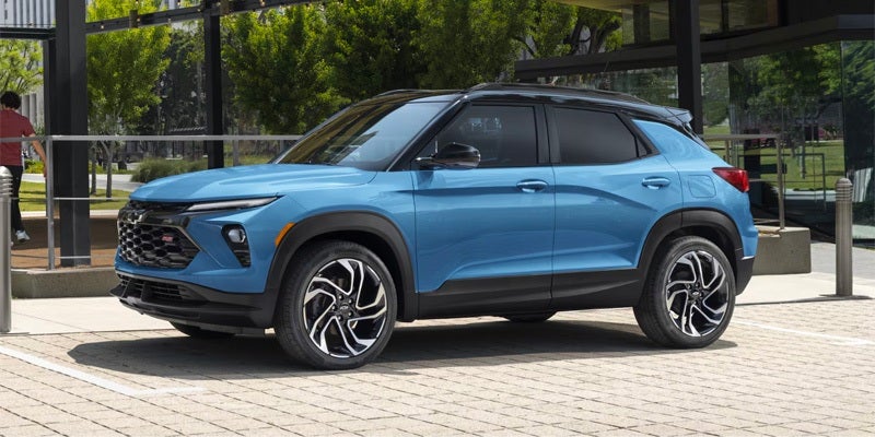 Light blue Chevrolet Trailblazer with a black roof parked on a paved lot beside a modern building.
