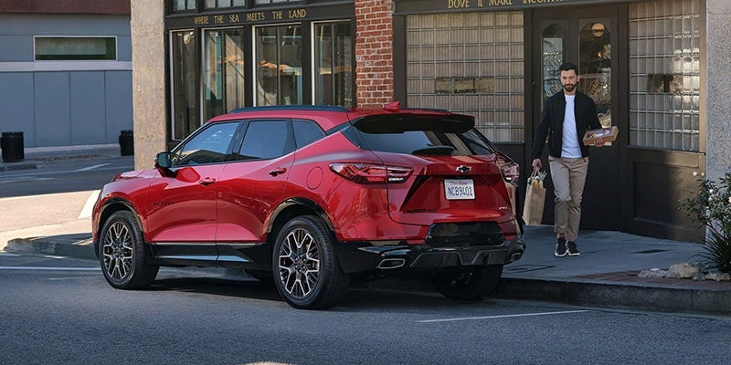 Rear view of a red Chevrolet Blazer parked on a street with a man carrying bags walking past it.
